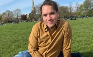 Clayton Grimm is sitting outside on the grass.