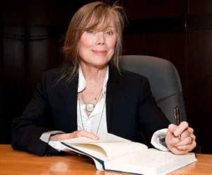 Sissy Spacek has a pen in her hand and a book on the table.