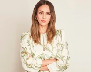 Jessica Alba is standing wearing a white dress.