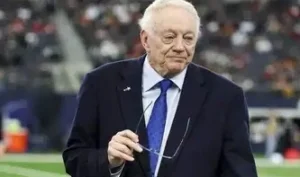 Jerry Jones stands in the ground, glasses in his hand.