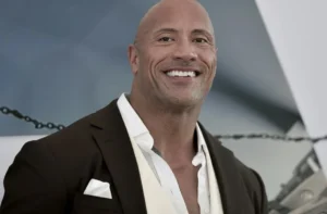 Man in a dark brown suit and white shirt smiling confidently at a formal event backdrop.