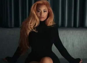 Nicki Minaj is sitting on a couch wearing black.