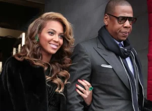 Jay Z's wife is holding his hand while laughing.
