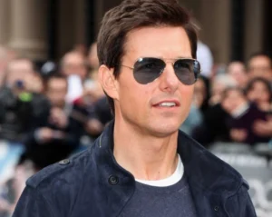 Tom Cruise is smiling while wearing dark glasses.