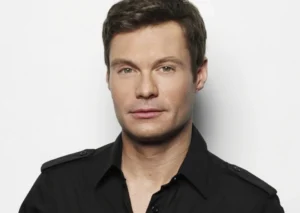 Ryan Seacrest is smiling while wearing black.