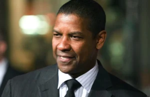 Denzel Washington stands outside, smiling.