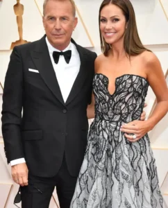 Kevin Costner is laughing while standing next to his wife.