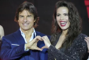 Tom Cruise and the girl are laughing while making a heart with their hands.