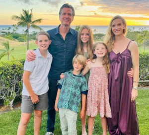 A happy family standing together in a garden during sunset, with the ocean and palm trees in the background.