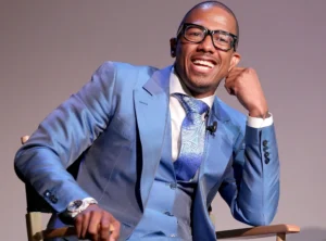 Nick Cannon is sitting in a chair, laughing.