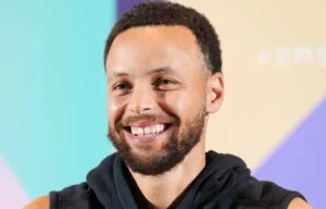 Stephen Curry is laughing while wearing a black sweater.