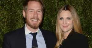 Drew Barrymore is laughing while standing next to her husband.