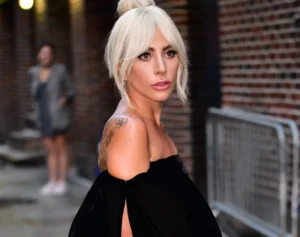 Lady Gaga is standing outside on the street, looking back.