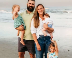Jason Kelce is standing on the beach with his wife and children, laughing.