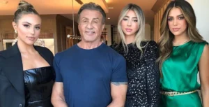 Sylvester Stallone is standing and smiling with his daughters.