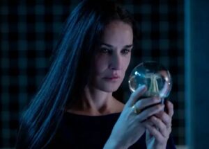 Woman with long dark hair wearing a black outfit, holding and staring at a glass orb with focus.