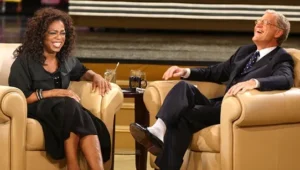 Oprah Winfrey and the man are laughing while sitting on the couch.