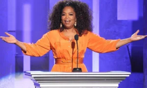 Oprah Winfrey is speaking into the microphone with her hands up.