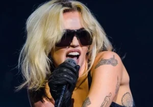 Miley Cyrus is singing into a microphone wearing gloves.