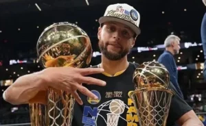 Stephen Curry holds two trophies in his hand.