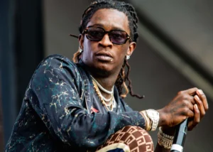 Young Thug Net is sitting with a microphone in his hand.
