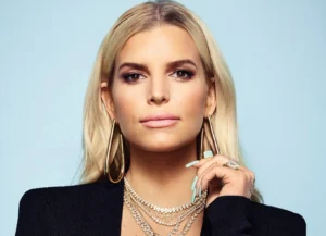 Jessica Simpson is wearing a black coat and smiling, showing off her big toenails.