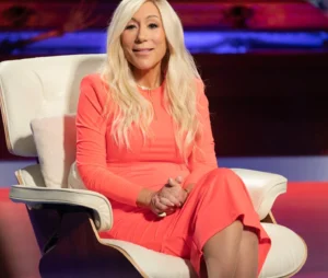 Lori Greiner is laughing while sitting on the couch wearing a pink dress.