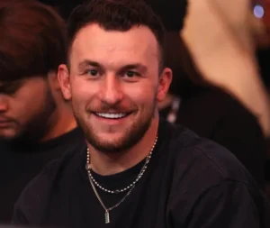 Johnny Manziel is laughing, wearing a black shirt and a chain around his neck.