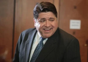 JB Pritzker is laughing, wearing a black coat.