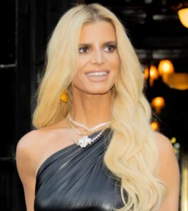 Jessica Simpson is laughing while wearing a black suit.