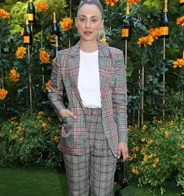 A woman wearing a checked suit with a white t-shirt, standing outdoors in front of a floral and champagne bottle display.