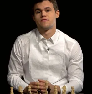 Magnus Carlsen is sitting dressed in white with a chess game in front of him.