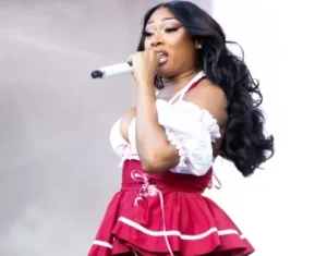 Megan Thee Stallion is singing into a microphone wearing a white and ivory frock.
