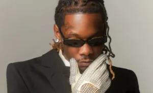 He is standing with his hands over his face, wearing an offset tunic.