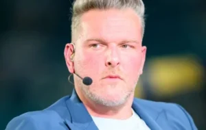 Pat McAfee is sitting in a blue coat with a microphone pressed to his face.