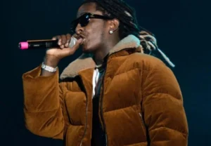 Young Thug is singing into a microphone wearing a yellow jacket.