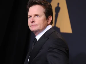 Michael J. Fox is looking up, wearing a black coat.