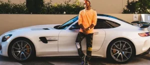 Lewis Hamilton is standing outside and a white car is parked behind.