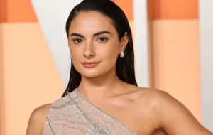 A woman with straight dark hair wearing a sparkly one-shoulder gown poses for a photo on the red carpet.