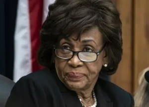 Maxine Waters is looking at someone wearing glasses.