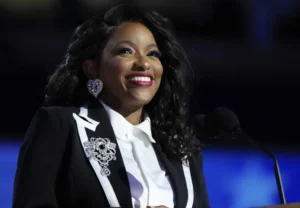 Jasmine Crockett laughs while speaking into a microphone while wearing a call coat.