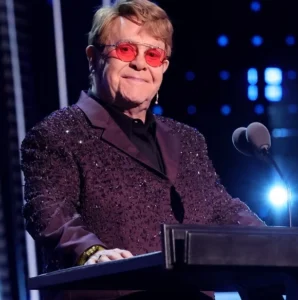 Elton John is laughing while talking into the mic.