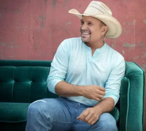 Garth Brooks is sitting on the couch, laughing while talking.