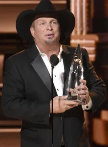 Garth Brooks speaks into the mic while holding the award.
