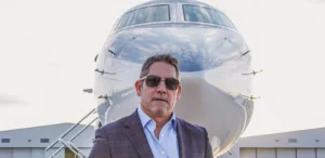 Grant Cardone stands in front of the ship, wearing dark glasses.