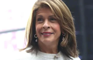 Hoda Kotb is standing outside wearing a white jersey.