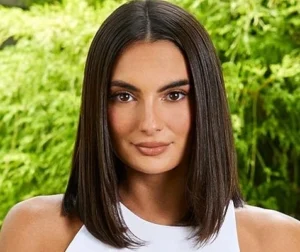 Paige de Sorbo is standing outside, dressed in white, smiling.