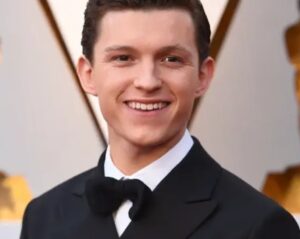 Man in a black tuxedo with a bow tie smiling on a red carpet event backdrop.